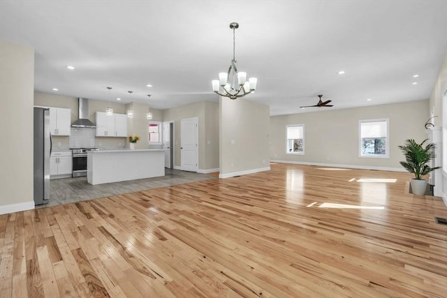 unfurnished living room featuring ceiling fan with notable chandelier, light wood-type flooring, baseboards, and recessed lighting