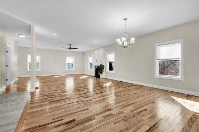 unfurnished living room with a warm lit fireplace, baseboards, ceiling fan with notable chandelier, light wood-type flooring, and recessed lighting