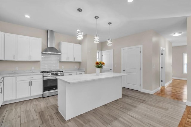 kitchen with white cabinets, wall chimney range hood, a center island, gas stove, and pendant lighting