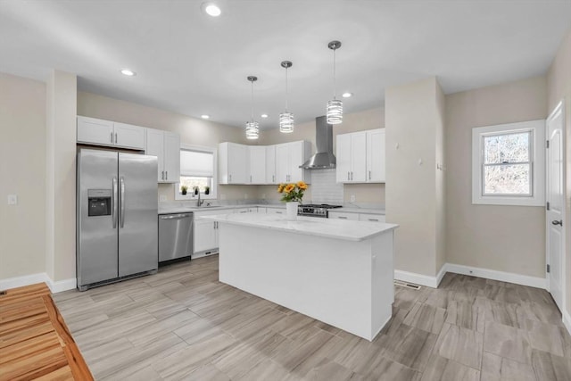 kitchen featuring appliances with stainless steel finishes, a kitchen island, wall chimney range hood, and white cabinetry