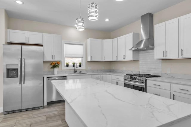 kitchen with decorative light fixtures, stainless steel appliances, white cabinetry, a sink, and wall chimney range hood