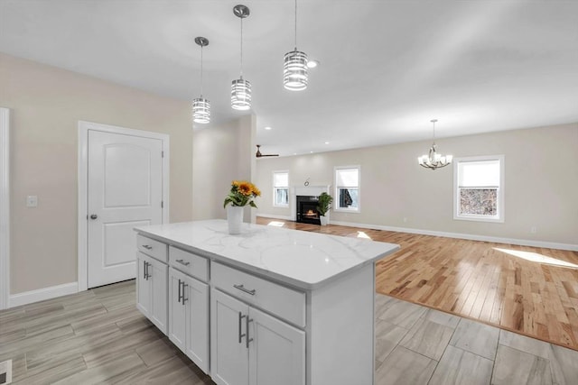 kitchen featuring a kitchen island, light stone counters, open floor plan, hanging light fixtures, and a lit fireplace