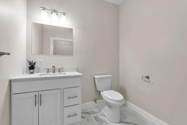 bathroom with toilet, marble finish floor, vanity, and baseboards