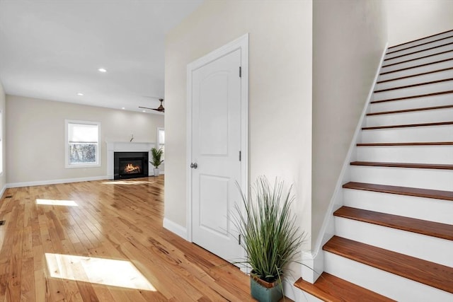 stairway with ceiling fan, hardwood / wood-style flooring, recessed lighting, a fireplace with flush hearth, and baseboards