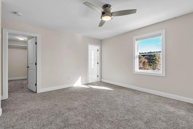 unfurnished bedroom featuring a ceiling fan, light carpet, a spacious closet, and baseboards