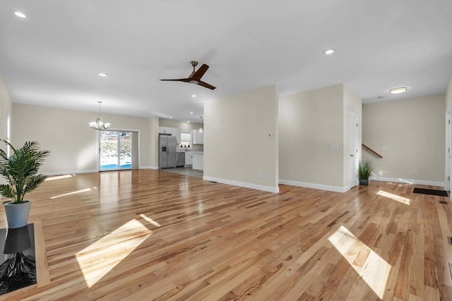 unfurnished living room with light wood-style floors, recessed lighting, baseboards, and ceiling fan with notable chandelier