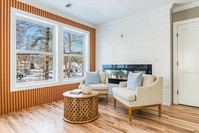 living area featuring a fireplace, crown molding, and light hardwood / wood-style flooring