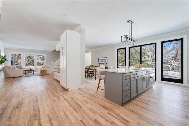 kitchen featuring white cabinetry, gray cabinets, a kitchen island with sink, pendant lighting, and a breakfast bar