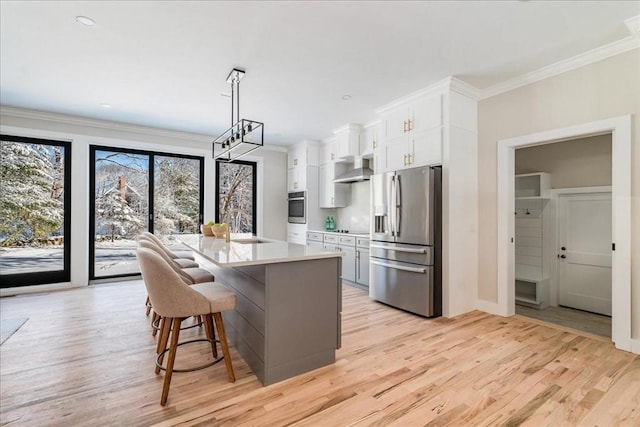 kitchen with appliances with stainless steel finishes, decorative light fixtures, white cabinetry, a kitchen breakfast bar, and a center island with sink