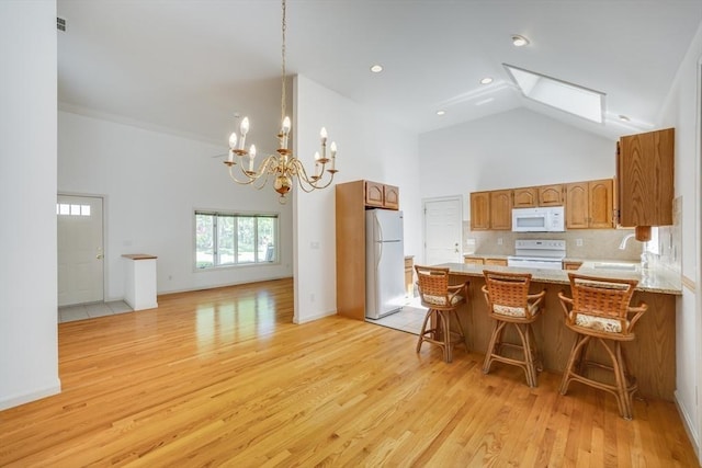 9 Dacey Dr, Barnstable, MA 02632 - kitchen with white appliances, high vaulted ceiling, brown cabinetry, light wood-style flooring, and a peninsula