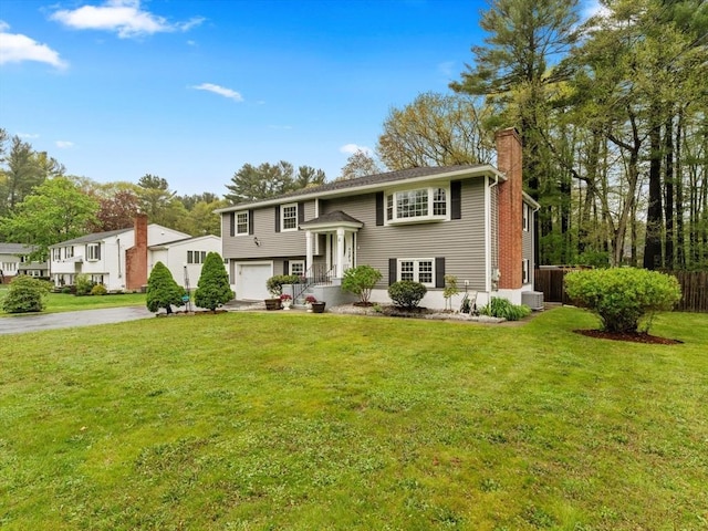 raised ranch with driveway, a chimney, central AC unit, and an attached garage