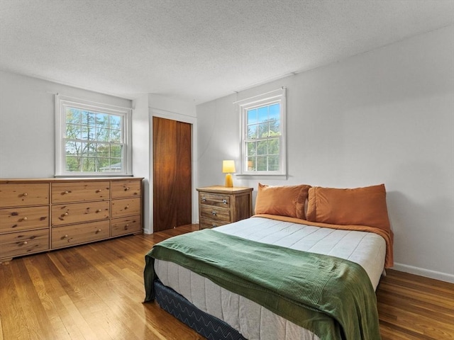 bedroom with wood finished floors, a textured ceiling, a closet, and baseboards