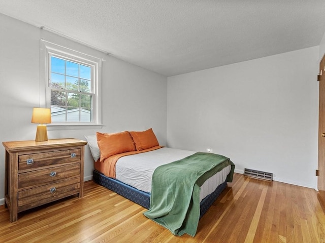bedroom with light wood finished floors, baseboards, and a textured ceiling