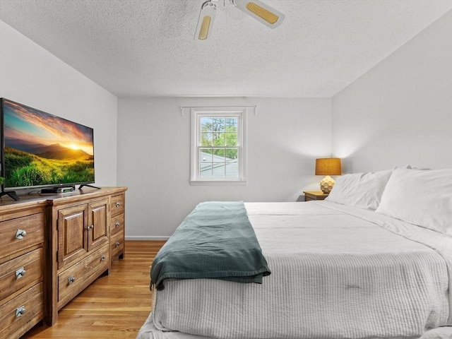bedroom with light wood finished floors, a textured ceiling, baseboards, and ceiling fan