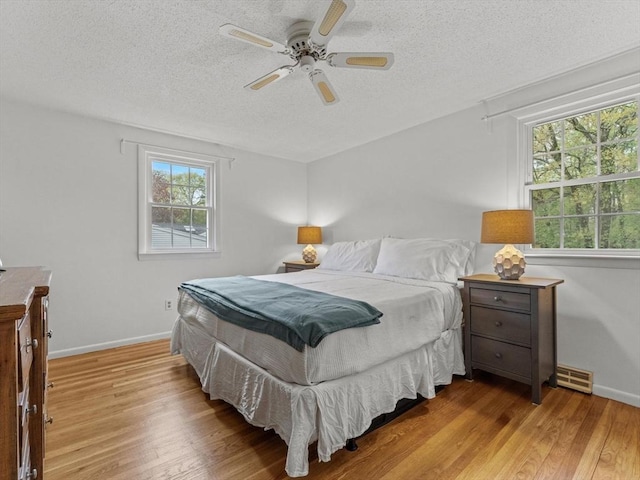 bedroom with a textured ceiling, wood finished floors, baseboards, and ceiling fan