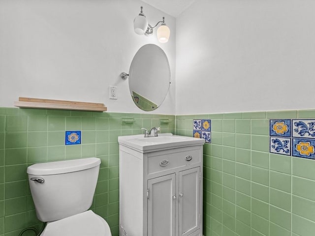 bathroom featuring tile walls, wainscoting, toilet, and vanity