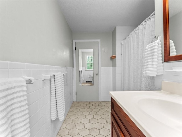 full bathroom with tile walls, a wainscoted wall, a textured ceiling, vanity, and tile patterned floors