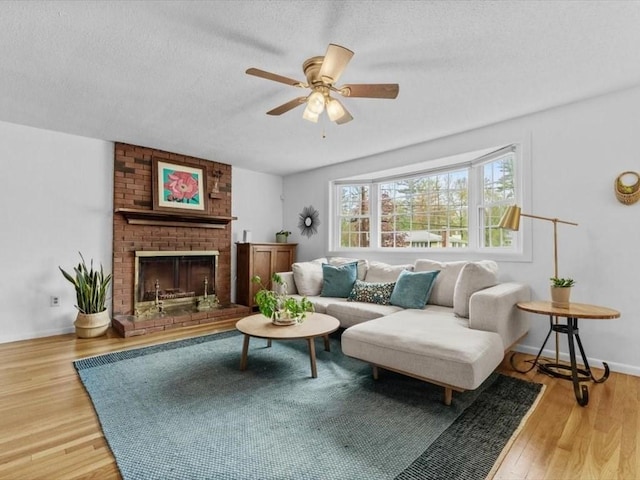 living room featuring ceiling fan, wood finished floors, a textured ceiling, a brick fireplace, and baseboards