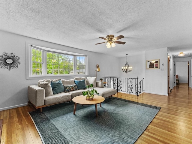 living area with wood finished floors, ceiling fan, a textured ceiling, baseboards, and a chandelier
