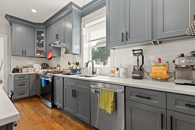 kitchen featuring gray cabinets, dark wood-type flooring, decorative backsplash, stainless steel appliances, and light stone countertops