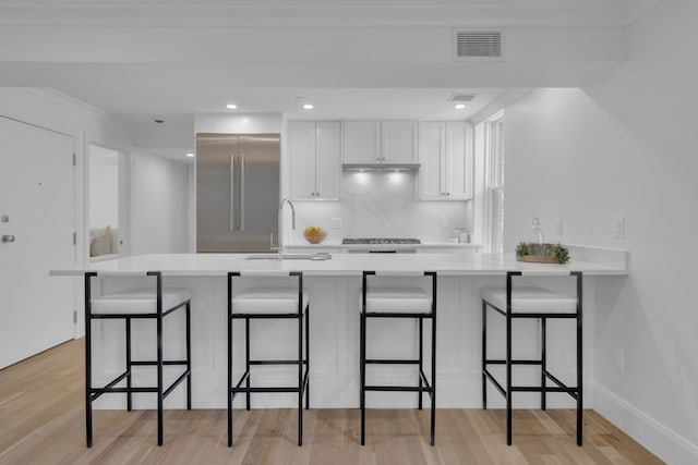 kitchen with appliances with stainless steel finishes, light hardwood / wood-style flooring, white cabinetry, sink, and a breakfast bar