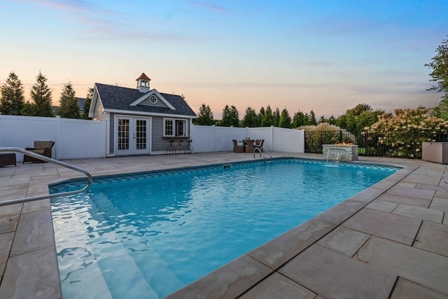 pool at dusk featuring an outbuilding, a patio area, and pool water feature