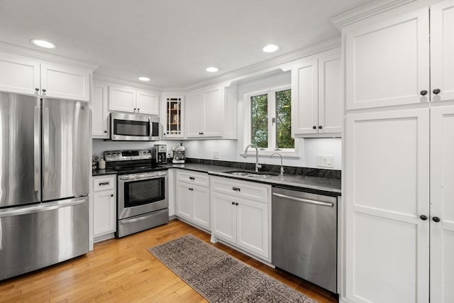 kitchen with appliances with stainless steel finishes, a sink, dark countertops, light wood-type flooring, and white cabinets