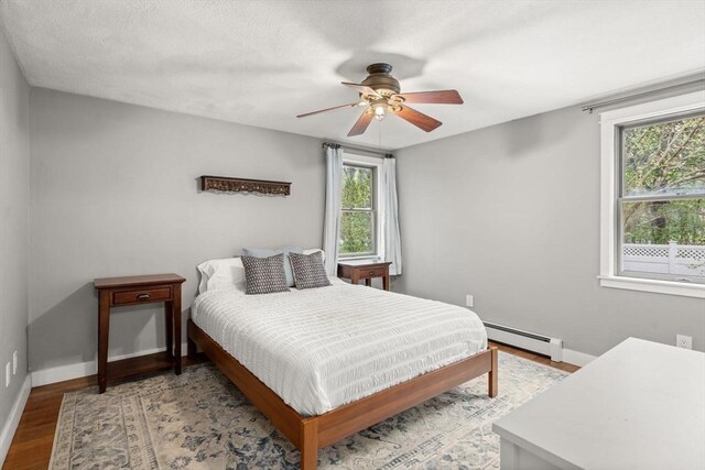bedroom featuring baseboard heating, wood finished floors, baseboards, and ceiling fan