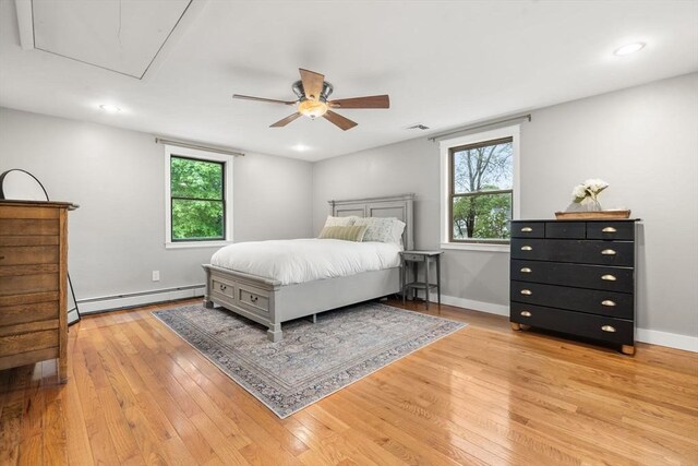 bedroom featuring a baseboard heating unit, attic access, multiple windows, light wood-type flooring, and recessed lighting