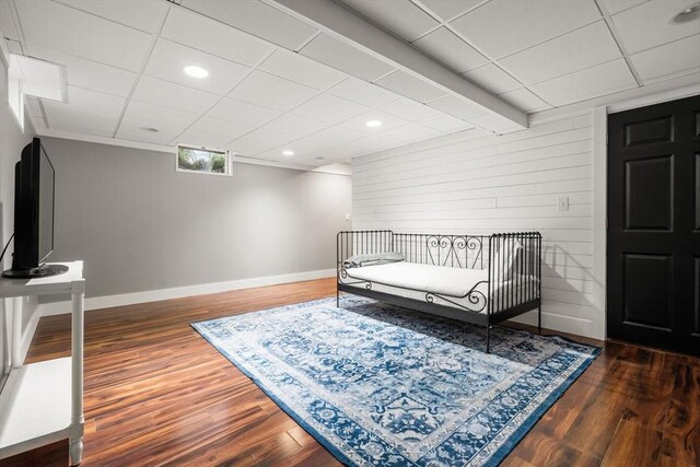 bedroom with baseboards, wood finished floors, wooden walls, recessed lighting, and a paneled ceiling