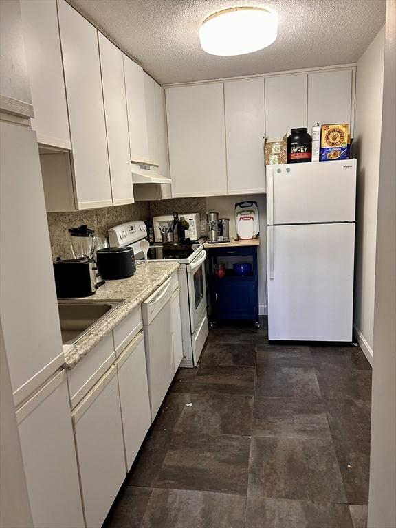 kitchen with under cabinet range hood, white appliances, a sink, and white cabinetry