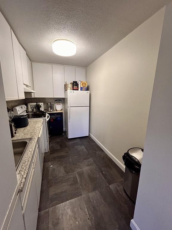 kitchen featuring freestanding refrigerator, a sink, stove, under cabinet range hood, and white cabinetry