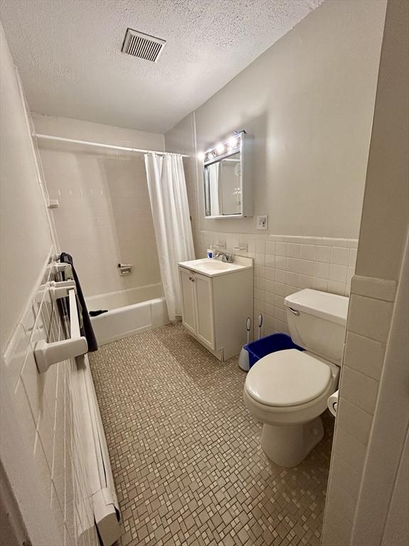 full bathroom featuring visible vents, tile walls, toilet, shower / tub combo, and a textured ceiling