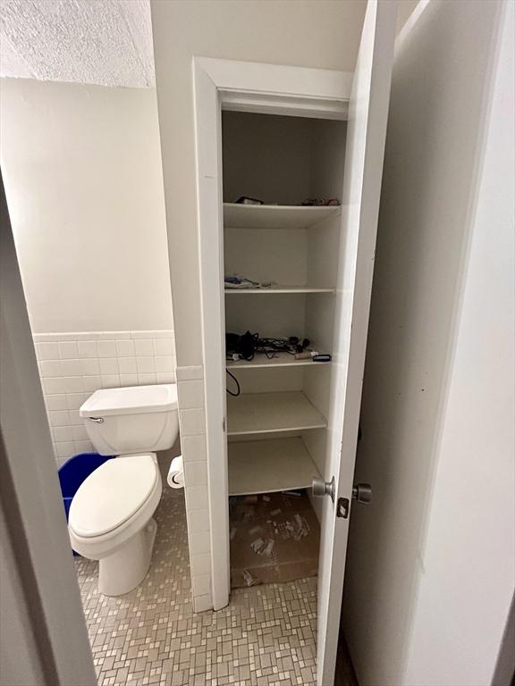 bathroom featuring tile walls, toilet, and a wainscoted wall