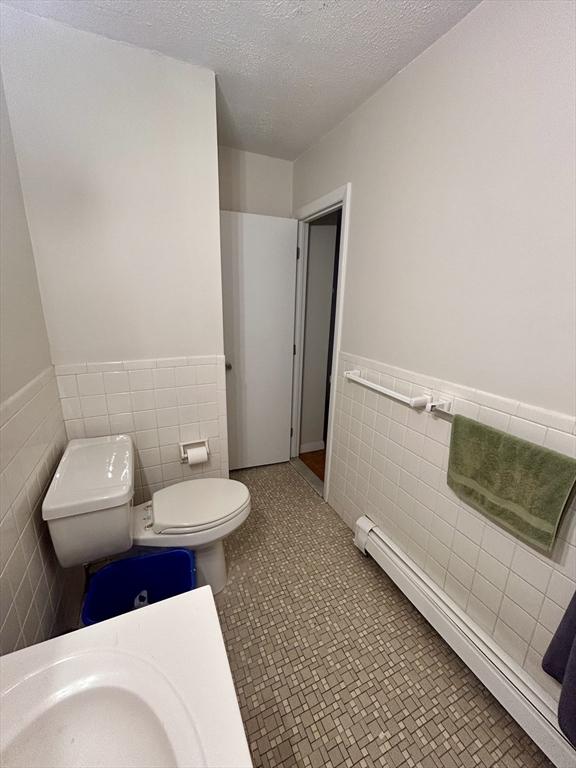 bathroom featuring a wainscoted wall, a textured ceiling, tile walls, and toilet