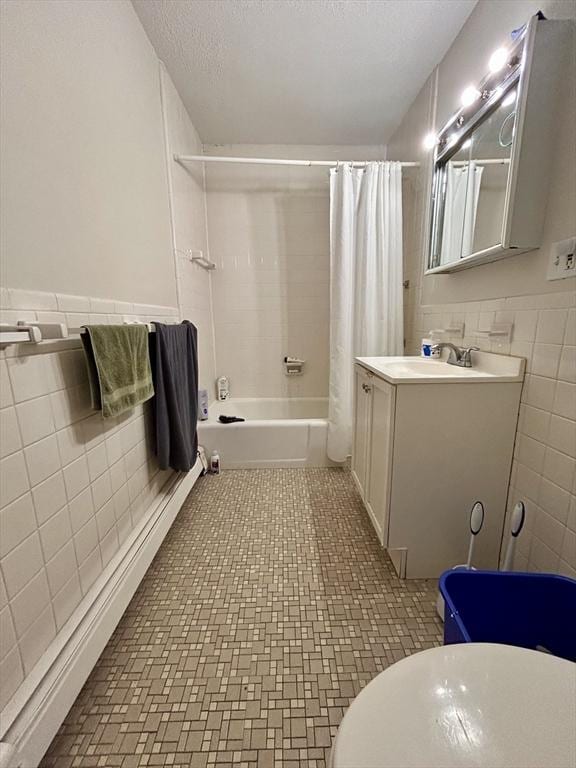 full bath featuring tile walls, vanity, wainscoting, a textured ceiling, and shower / bathtub combination with curtain