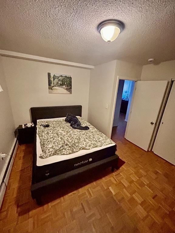 bedroom featuring a baseboard heating unit, a textured ceiling, and parquet flooring