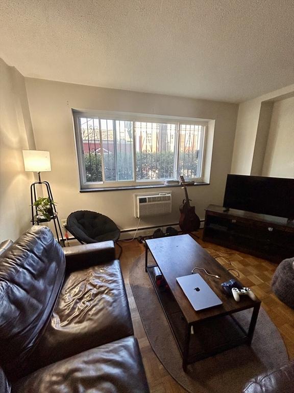 living area featuring baseboard heating, a textured ceiling, and an AC wall unit