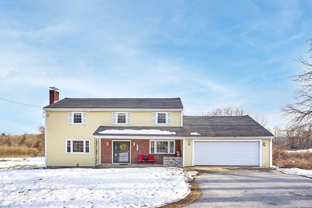 traditional home with aphalt driveway, brick siding, a chimney, and an attached garage