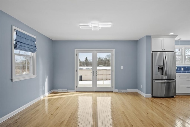 interior space with light wood-type flooring, visible vents, baseboards, and french doors