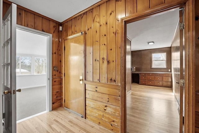 hallway featuring wood walls, baseboards, and light wood finished floors