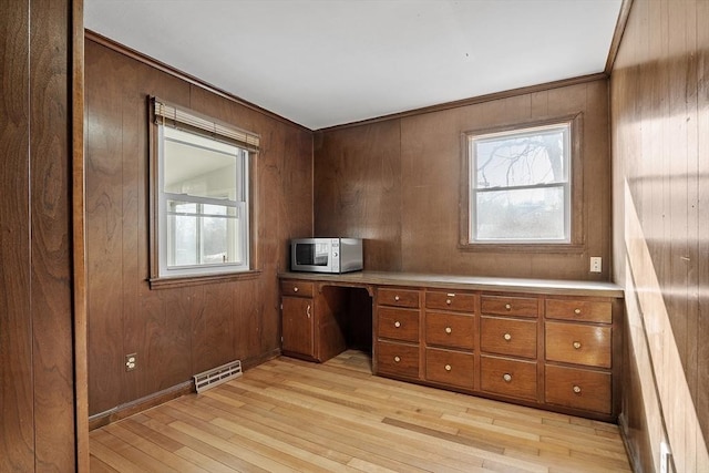 unfurnished office with built in desk, light wood-style floors, visible vents, and a wealth of natural light