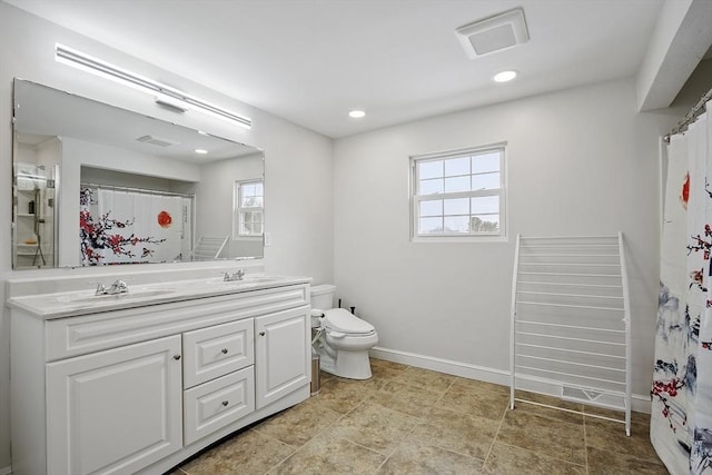 bathroom with double vanity, a sink, toilet, and a healthy amount of sunlight