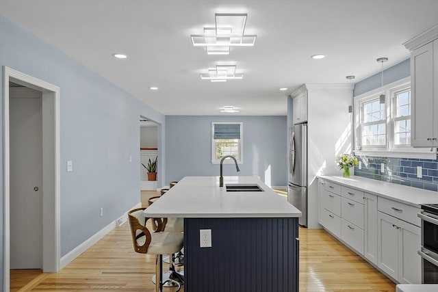 kitchen featuring tasteful backsplash, light wood-style floors, a sink, an island with sink, and stainless steel fridge