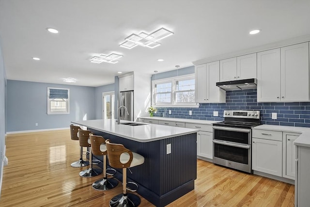 kitchen featuring a kitchen island with sink, under cabinet range hood, light wood-style floors, appliances with stainless steel finishes, and a kitchen bar