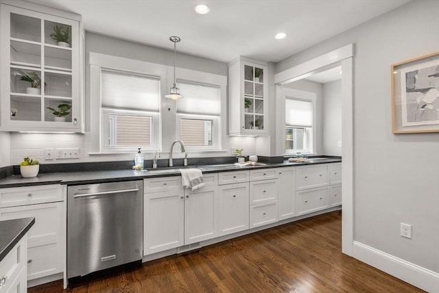 kitchen with dark wood-style flooring, dark countertops, stainless steel dishwasher, a sink, and white cabinetry