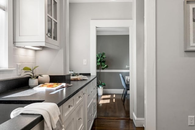 kitchen featuring glass insert cabinets, dark countertops, dark wood finished floors, and white cabinetry
