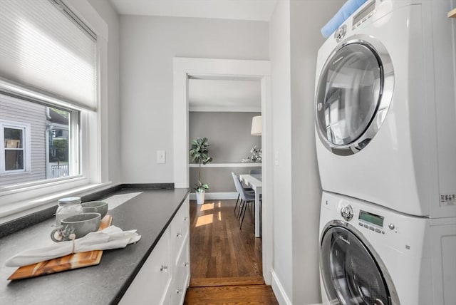 laundry room featuring cabinet space, stacked washer / drying machine, baseboards, and wood finished floors