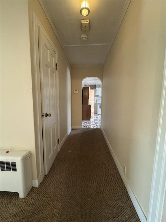 hallway featuring arched walkways, radiator, carpet, and baseboards