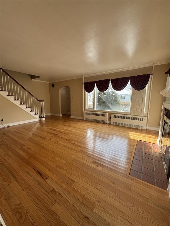 unfurnished living room featuring arched walkways, radiator, a glass covered fireplace, and stairs